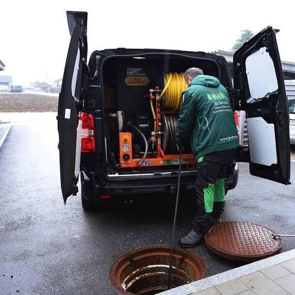 Mitarbeiter von JP-Service spült eine Grundleitung über den Kanalschacht mit Hochdruck